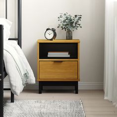 a nightstand with a clock and books on it next to a bed in a bedroom