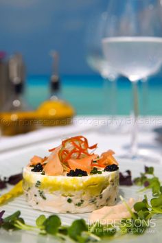 a white plate topped with an appetizer next to a wine glass and water