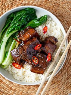 a bowl filled with meat and vegetables next to chopsticks on top of rice