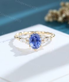 a tan gold ring with an oval blue sapphire surrounded by small white diamonds on a card