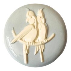 a white ceramic bird on top of a gray and white plate with two smaller birds sitting on it's back legs