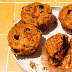 four muffins on a white plate sitting on a yellow tile floor next to each other