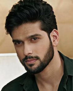 a close up of a person with a beard and black shirt in front of a wall