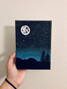 a hand holding up a small card with the moon and trees painted on it