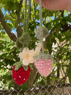 two crocheted strawberries hanging from a chain in front of a tree with leaves