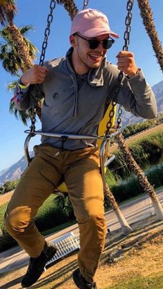 a man is sitting on a swing with his hands in the air while wearing sunglasses and a pink hat