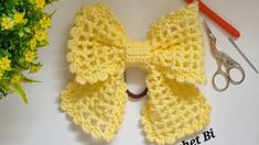 a crocheted yellow bow sits next to a pair of scissors and some flowers