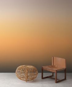 an empty chair and a wooden stool in front of a wall with a sunset behind it