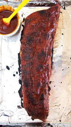 a piece of meat sitting on top of tin foil next to a bowl of ketchup