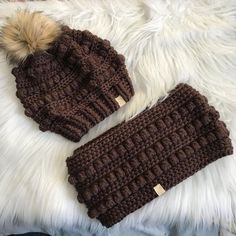 two crocheted hats laying on top of a white fur rug next to each other