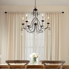 a chandelier hangs over a dining room table with two chairs and a vase filled with flowers