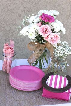 pink and white flowers are in a mason jar with plates, napkins, and utensils