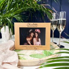 a photo frame sitting on top of a table next to two wine glasses and palm leaves