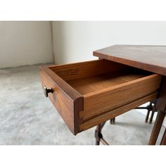 a wooden desk with an open drawer on it's top and two stools in the background