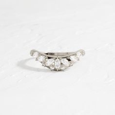 a white gold ring with three pear shaped diamonds on it's sides, sitting on a plain surface