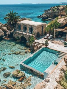 an outdoor swimming pool surrounded by rocks next to the ocean with a stone house in the background