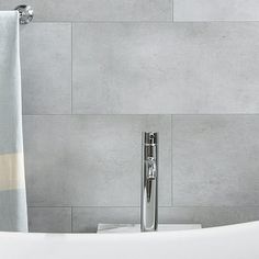 a white bath tub sitting next to a shower curtain in a bathroom with grey tiles on the wall