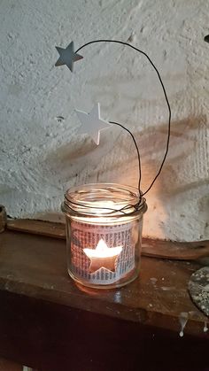 a glass jar filled with stars on top of a wooden table next to a candle