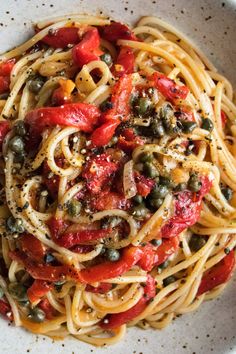 a white bowl filled with pasta, olives and tomatoes on top of a table