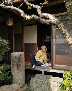 a woman sitting on a bench in front of a building with trees and rocks around her