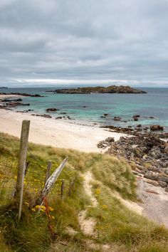 a sandy beach next to the ocean under a cloudy sky