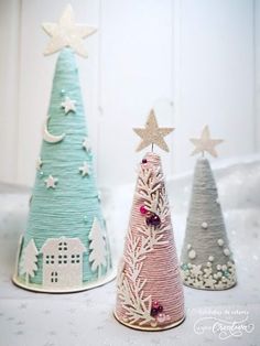 three small christmas trees made out of yarn with stars on top and houses in the background