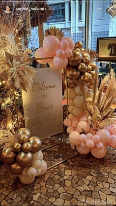 a welcome sign and balloons are on display in a store window with gold, white and pink decorations