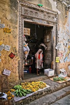 a woman standing in the doorway of a store with bananas and other items on display