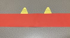 a piece of red paper with two yellow cats on it's head and one has been cut out