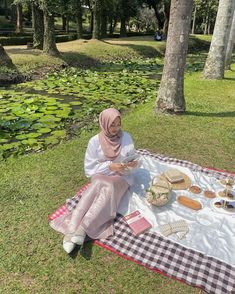 a woman sitting on the grass with food in front of her and some water lilies