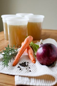 carrots, onions and other vegetables sit on a table next to cups of liquid