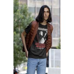 a man with long hair wearing a t - shirt and jeans standing in front of a building