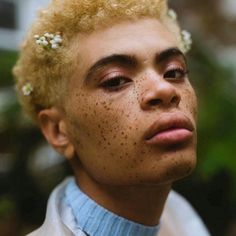 a man with freckled hair wearing a blue shirt and white flowers in his hair