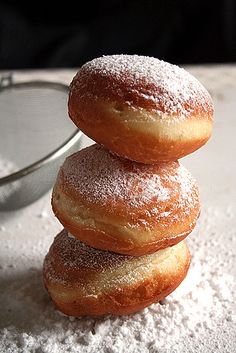 three donuts stacked on top of each other in front of a glass bowl filled with powdered sugar