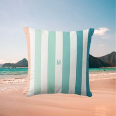 a blue and white striped pillow sitting on top of a sandy beach