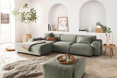 a living room with an l shaped couch and coffee table in the corner, along with potted plants