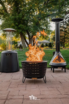 a fire pit sitting on top of a brick patio next to two black tables and chairs