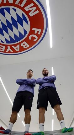 two men standing in front of the logo of a soccer team, with their arms wrapped around each other