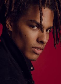 a young man with dreadlocks on his head looking at the camera while standing against a red background