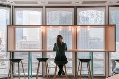 a woman sitting at a bar with three stools in front of her and looking out the window