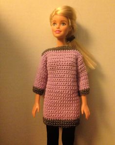 a doll is standing next to a wall wearing a crocheted dress and black pants