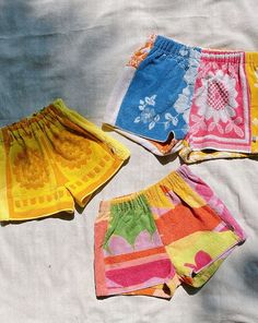 four different colored shorts laying on top of a white sheet next to an orange, yellow, and blue towel