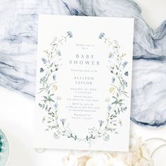 a baby shower with flowers and greenery on the front, next to a blue plate