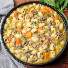 a bowl filled with pasta and meat soup on top of a wooden table next to a spoon