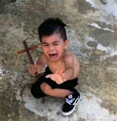 a young boy sitting on the ground with a cross in his hand and making a face