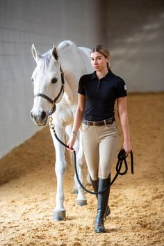 a woman is walking her horse in an indoor area with sand and grass on the ground