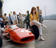 a woman sitting on top of a red race car in front of a group of people