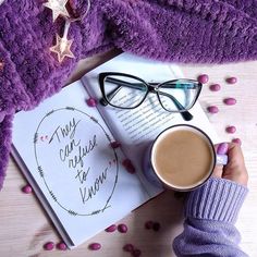 a person holding a cup of coffee next to an open book