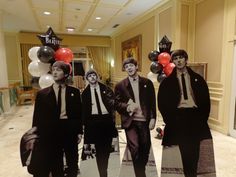 four men in suits and ties are walking down the hall with balloons on their heads