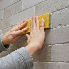 a person cleaning a brick wall with a sponge on the side and hand reaching for it